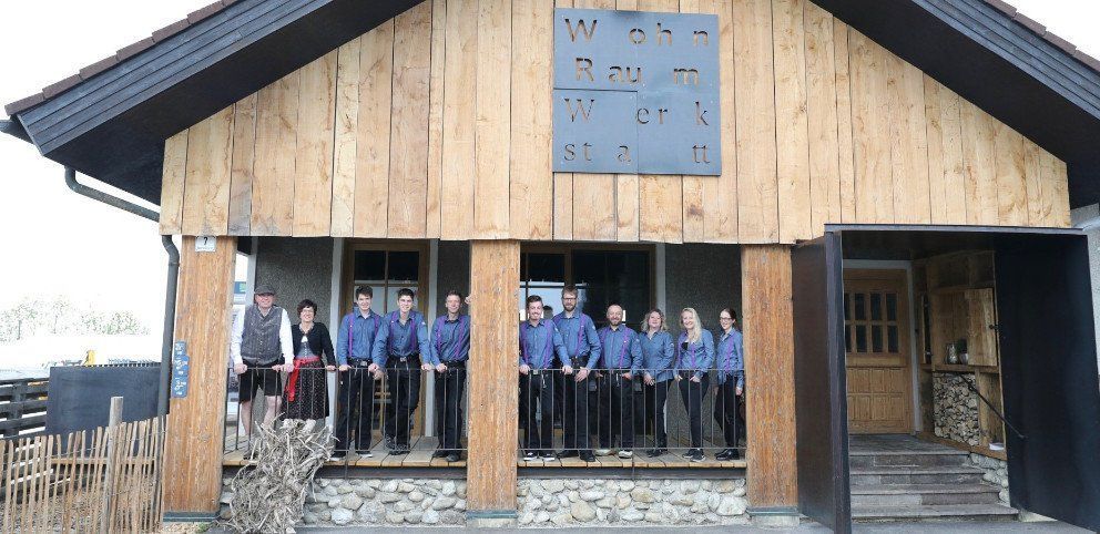 Eine Gruppe von Menschen steht unter einem hölzernen Pavillon mit einem blauen Schild über dem Eingang.