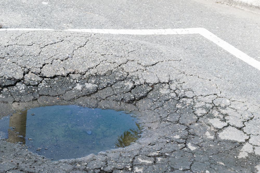 Cracked asphalt road with a pothole filled with water and faded white lane markings