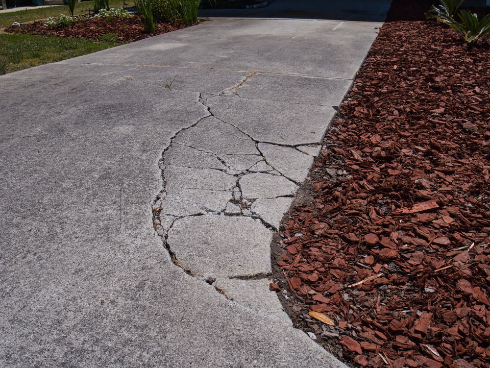 Cracked concrete driveway beside a bed of brown mulch.