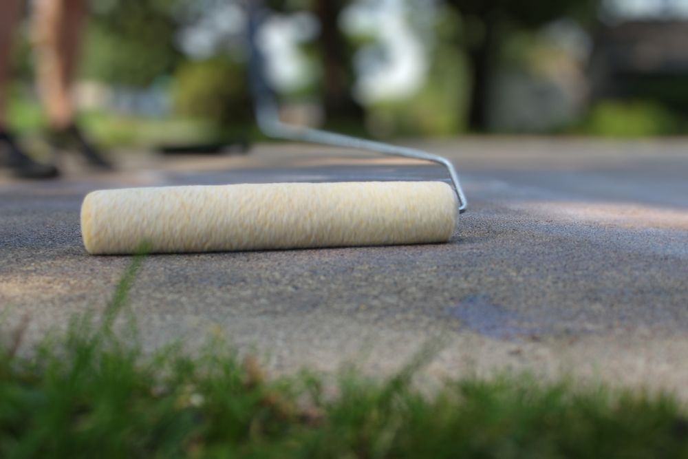 Paint roller on a pavement, lying on its side outdoors with a blurred background