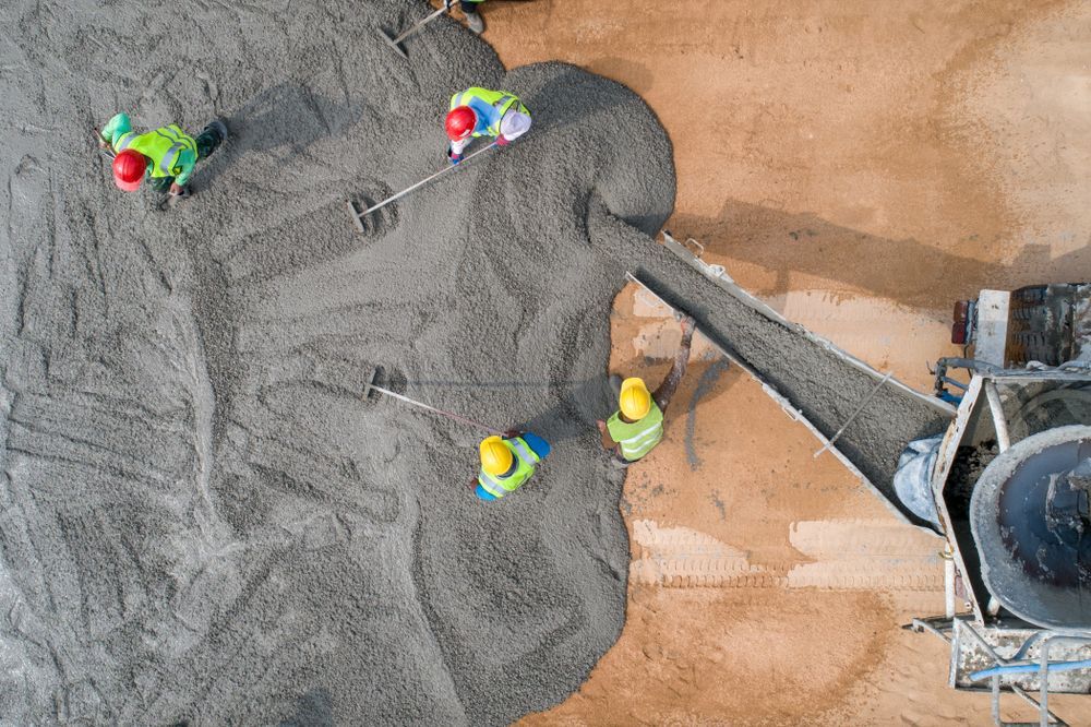 Workers pouring concrete from a machine onto a construction site.