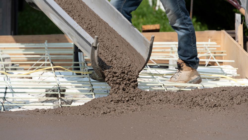 Concrete pouring from a chute onto rebar at a construction site, with workers’ legs visible.