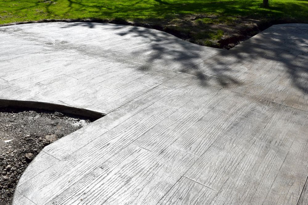 Gray concrete patio with wood grain pattern, near grass and gravel.