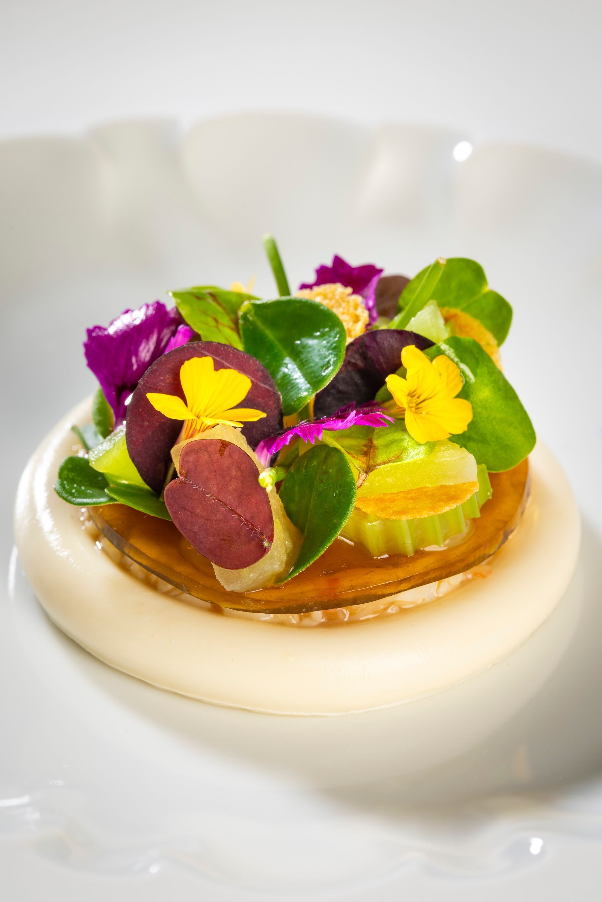 Gourmet dessert tart topped with colorful edible flowers and fruit on a white plate