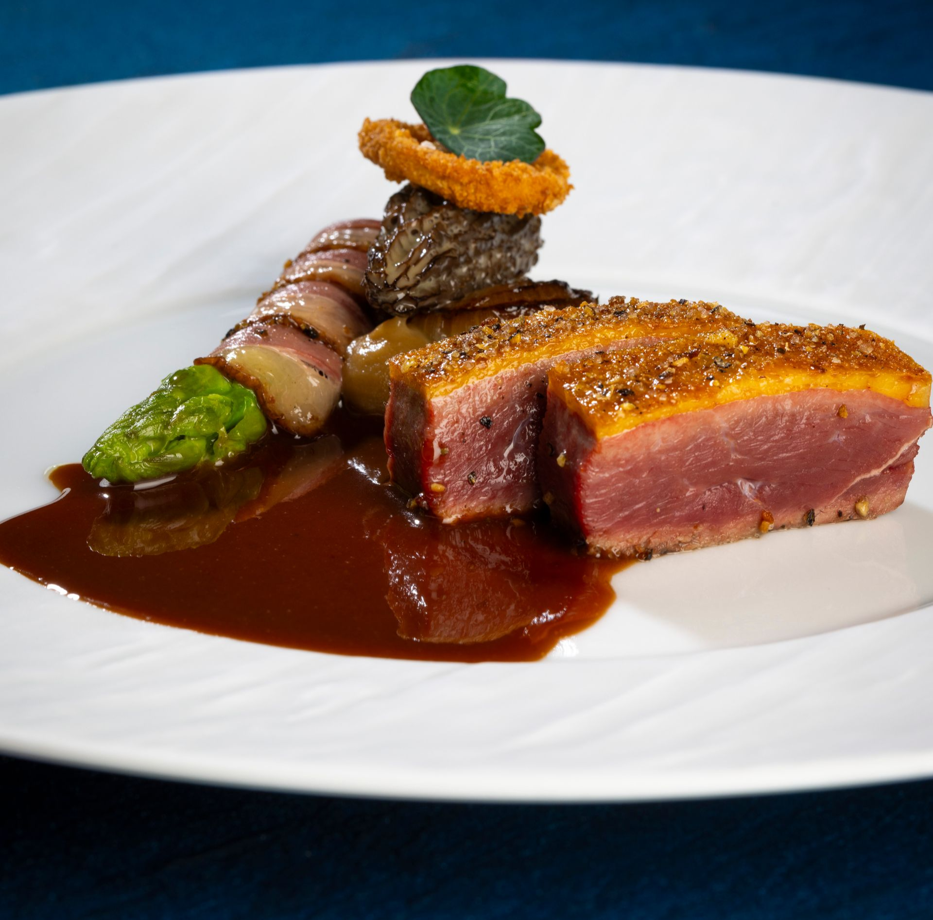 Seared steak with sauce, asparagus, and garnished vegetables on a white plate