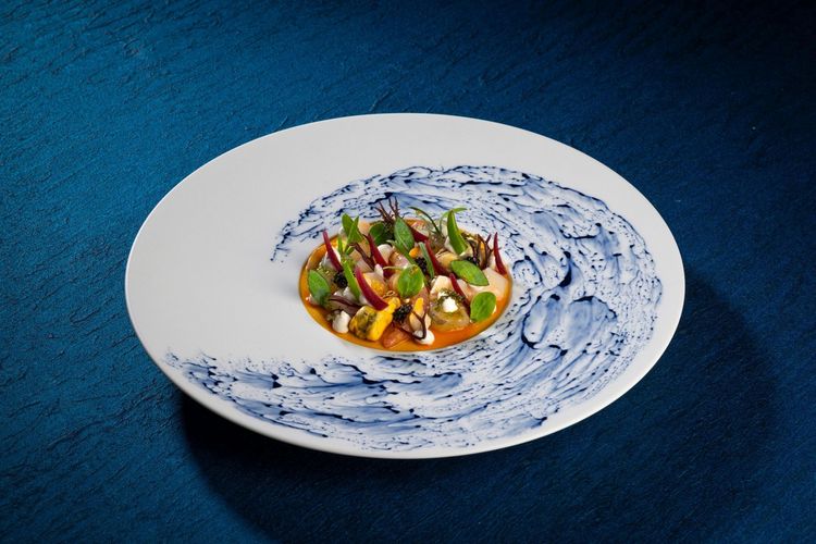 White plate with colorful food and blue sauce swirl on a dark blue tablecloth