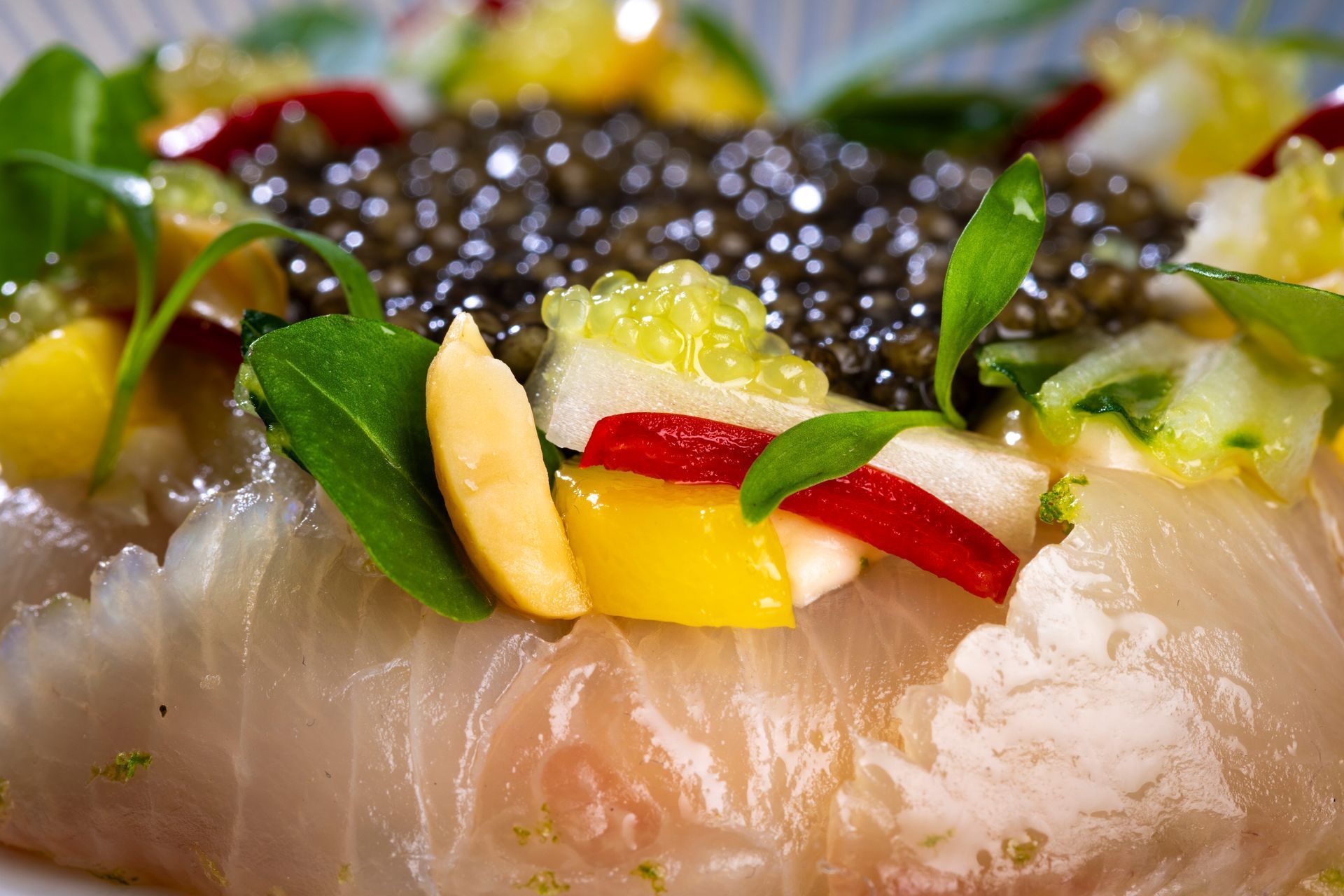 Close-up of sliced sashimi topped with black caviar and colorful garnishes on a plate