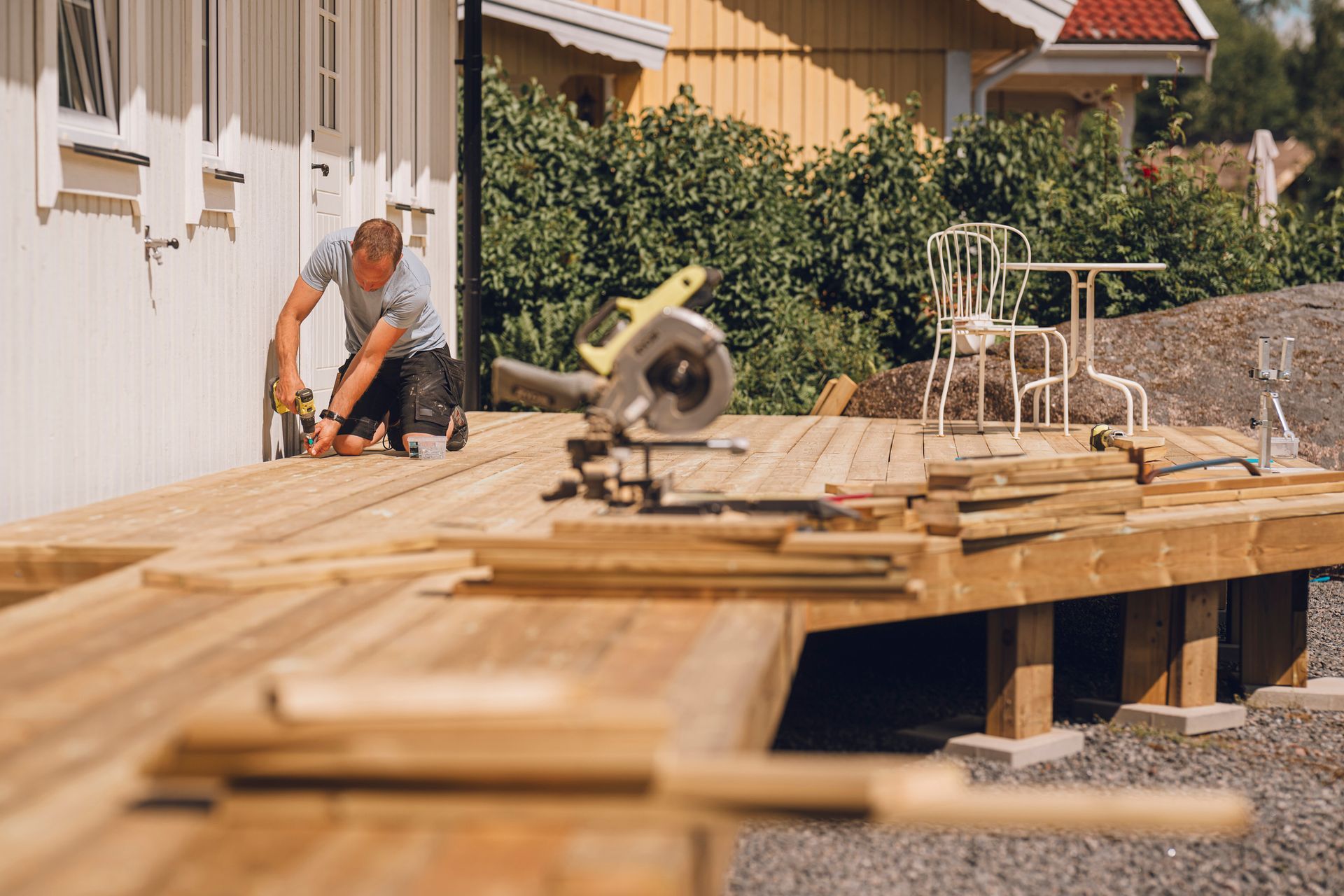 A man is working on a wooden deck in front of a house. A man is working on a wooden deck in front of a house.