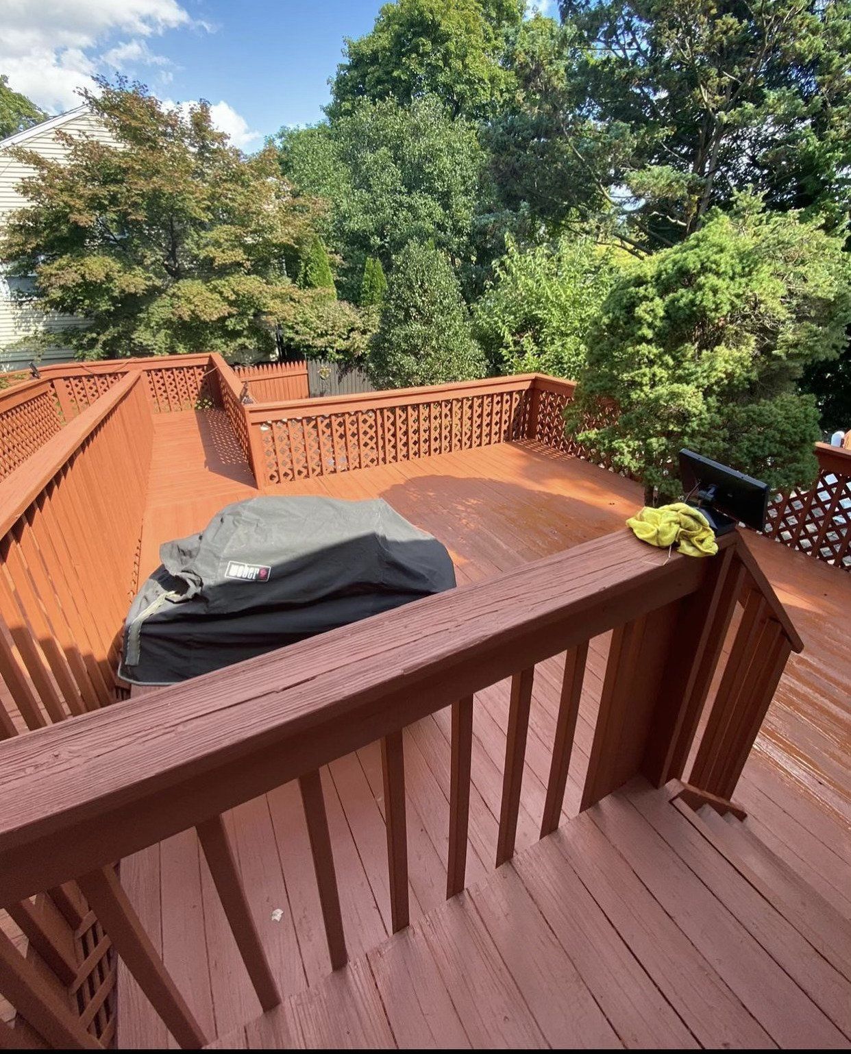 Brown wooden deck with grill covered and green trees.