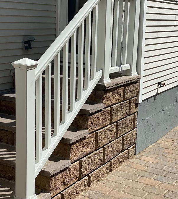 White railing and steps lead up from brick patio, adjacent to a brick retaining wall against a light-colored building.