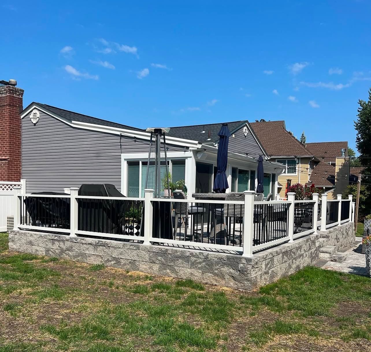 A house with a black and white deck on a stone foundation, under a blue sky.