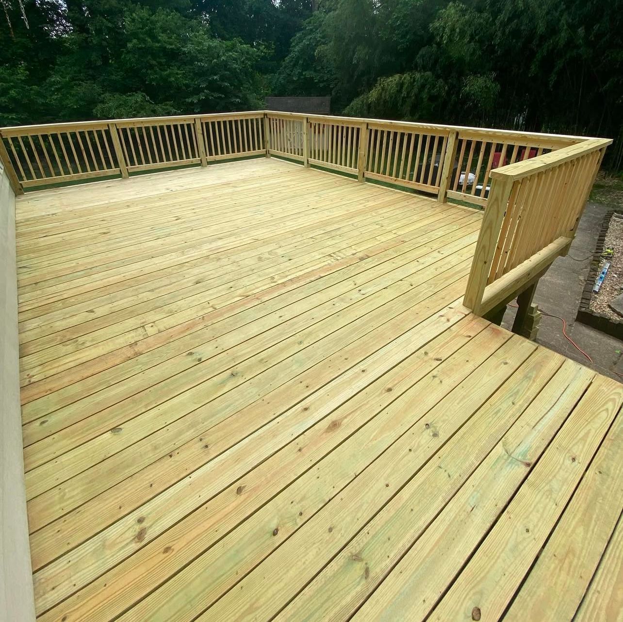 Wooden deck with railing, in backyard, light-colored wood.