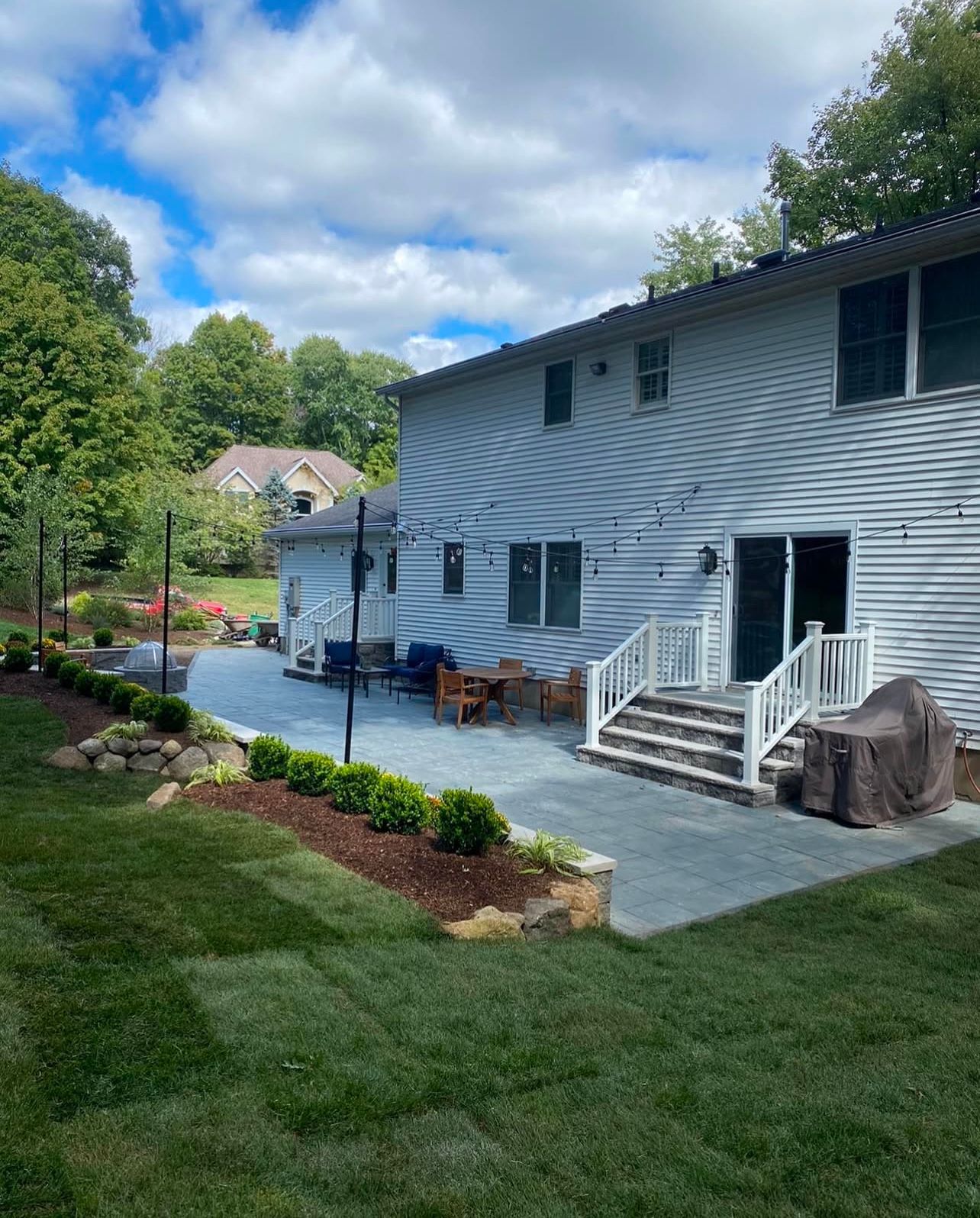 Backyard patio with lawn, steps, and house under a cloudy sky.