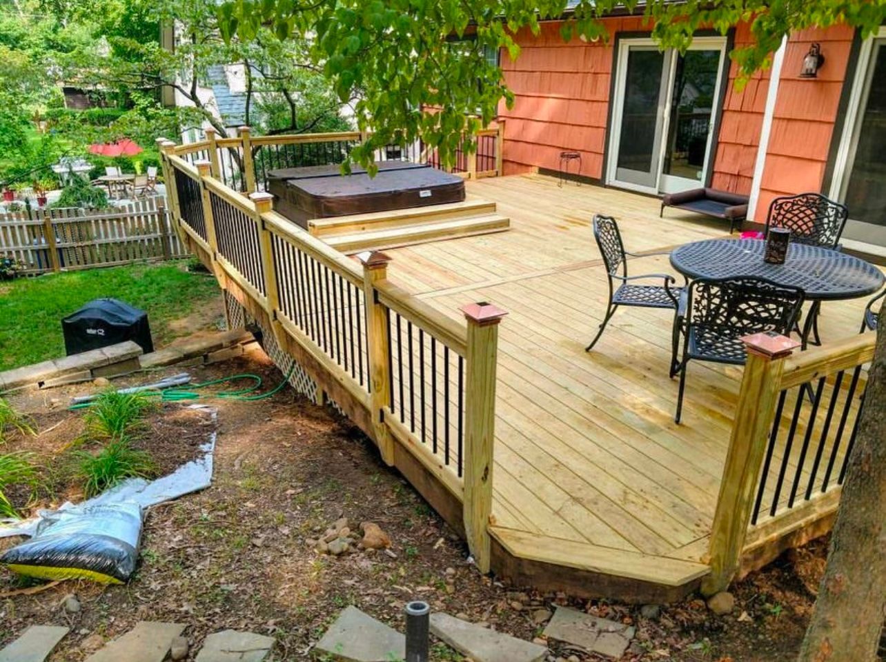 Wooden deck with hot tub, seating area, and railings, next to a house and a yard.