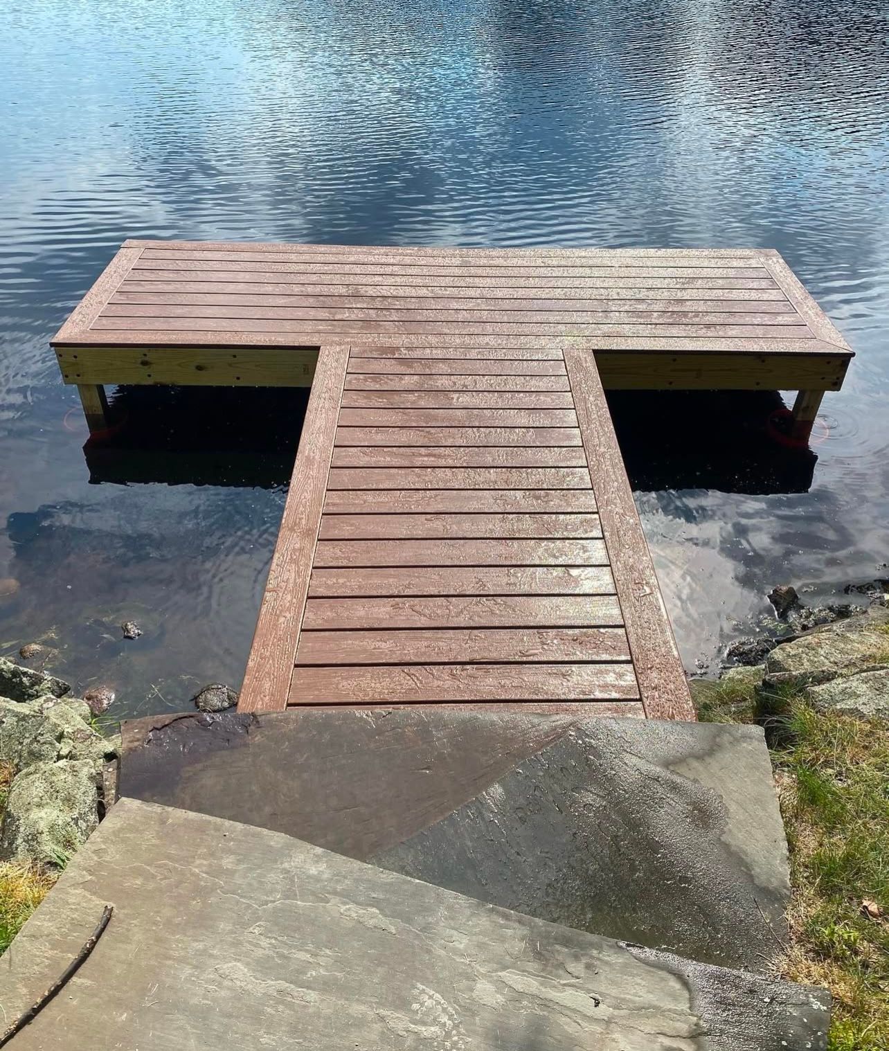 Brown wooden dock extending into a lake. Concrete steps lead down to the dock.