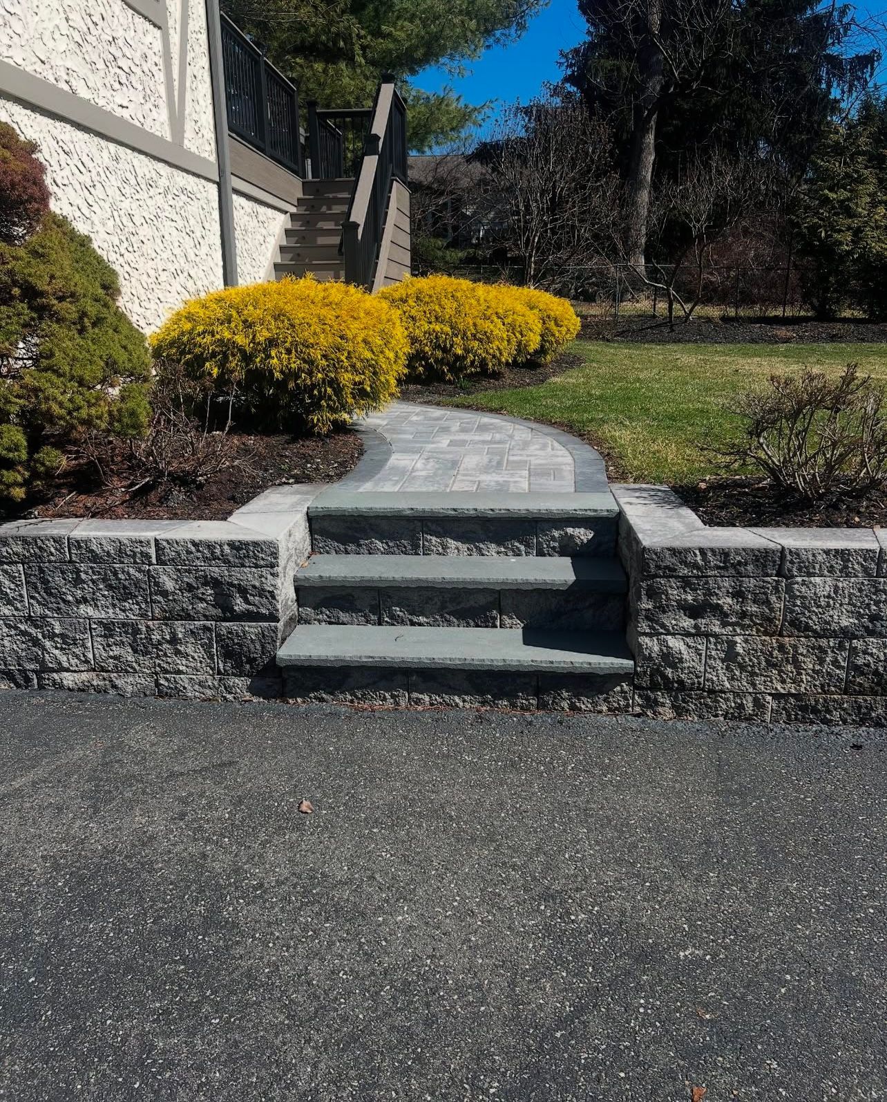 Stone steps leading up to a walkway, flanked by stone walls and yellow bushes.
