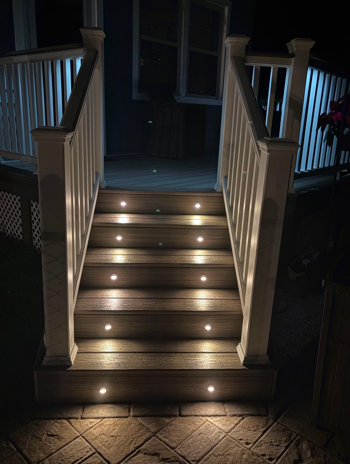 Wooden outdoor stairs with built-in lights. White railings frame the steps at night.
