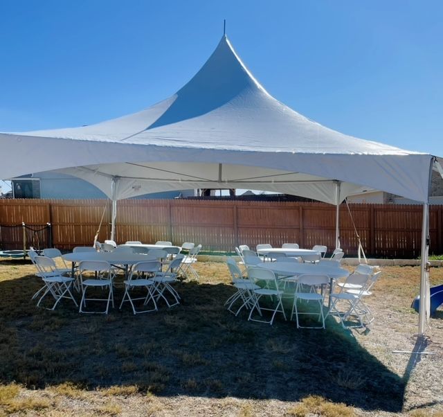 A white high-peak tent set up on a grass lawn, containing several round tables and white folding chairs.