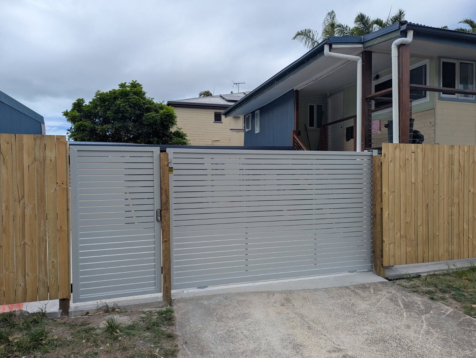 Aluminium Driveway Gate Beside a Wooden Fence — A & B Lattice World & Patios in Bungalow, QLD