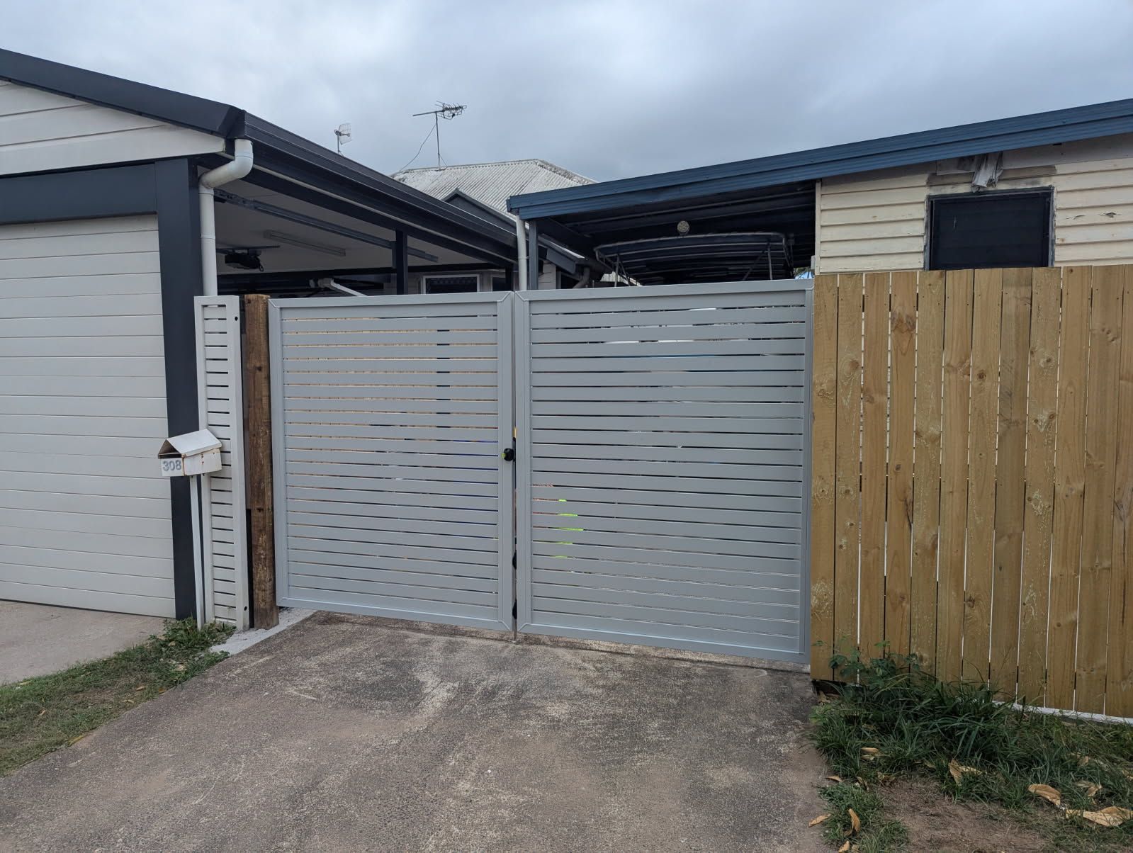 A White Gate Is Open to A Driveway in Front of A House — A & B Lattice World & Patios in Bungalow, QLD