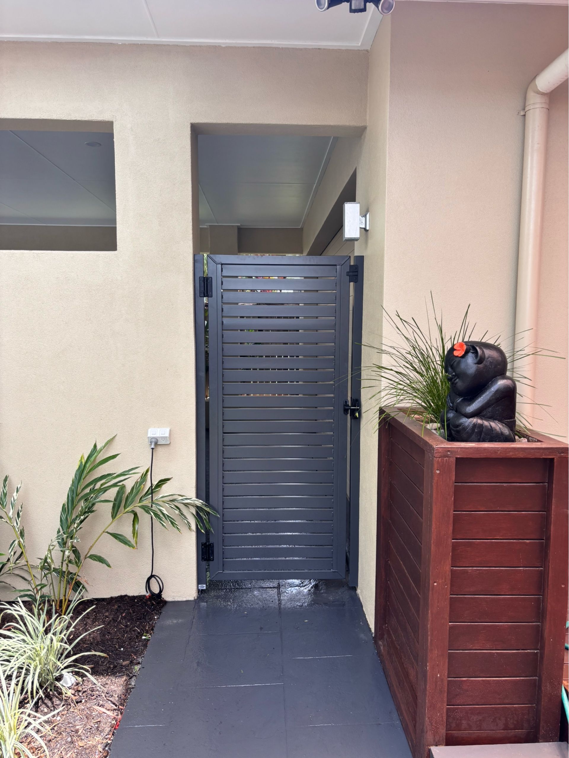 Front entryway with gray gate, beige walls, potted plants, and a wooden planter topped with a black cat statue.