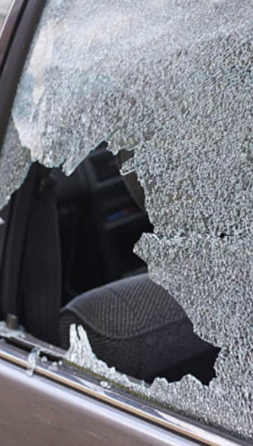 Shattered car side window with a large hole and broken glass fragments