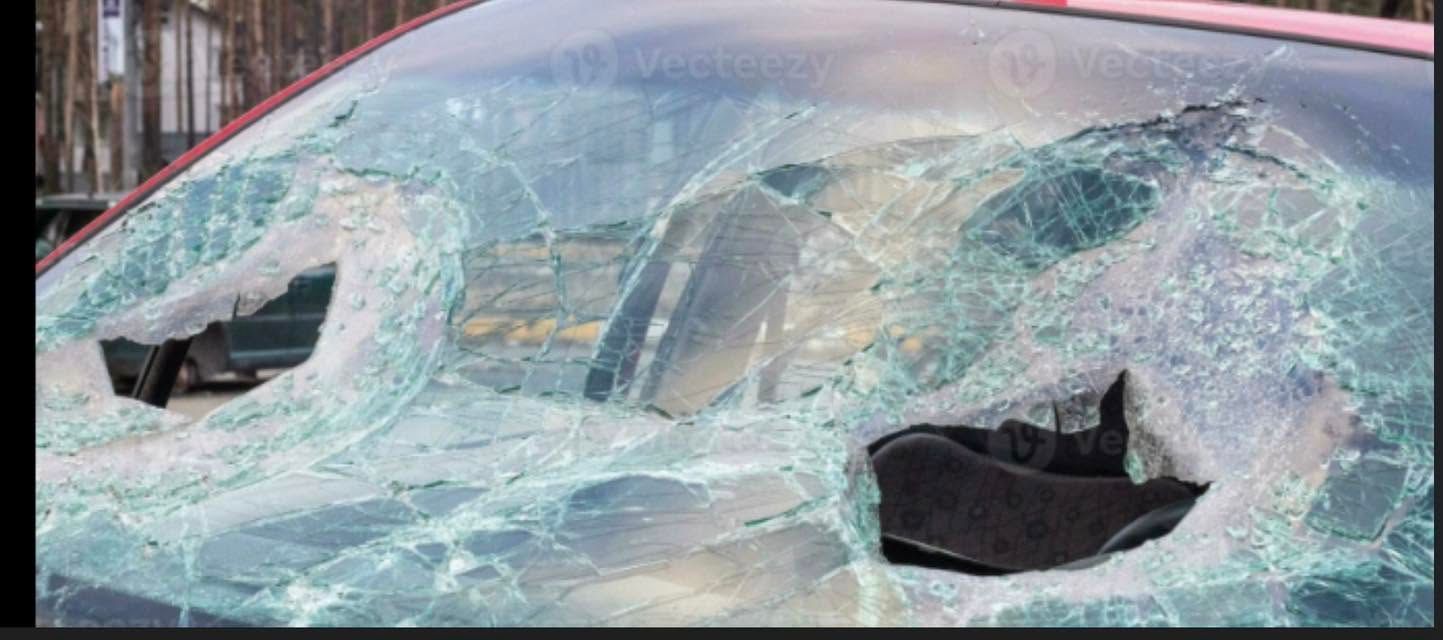 Shattered car windshield with two large holes and spiderweb cracks across the glass