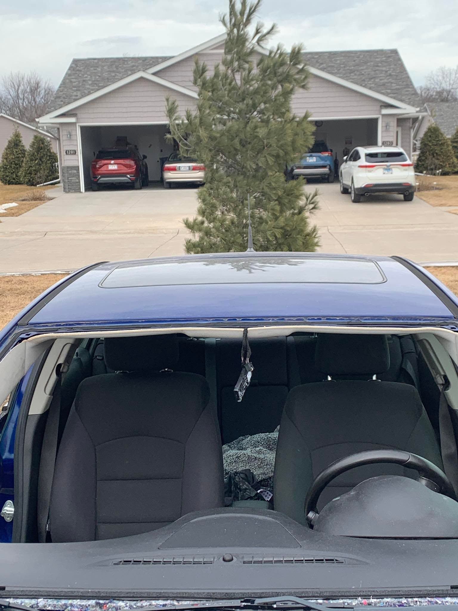 Blue car in a driveway with a house and open garage in the background.