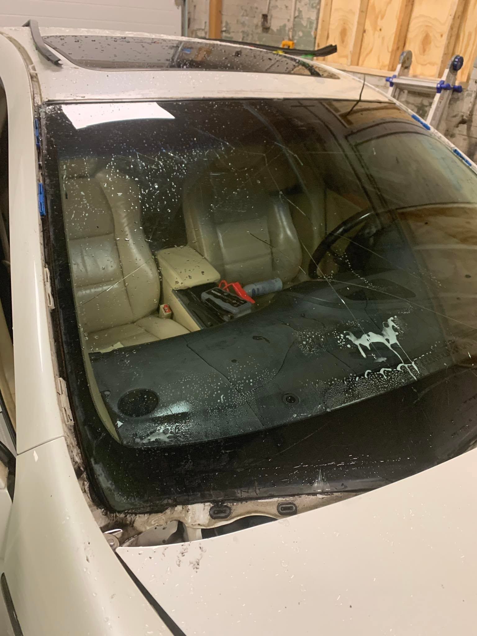 White car windshield covered in water droplets and broken glass, with airbag deployed inside a garage.