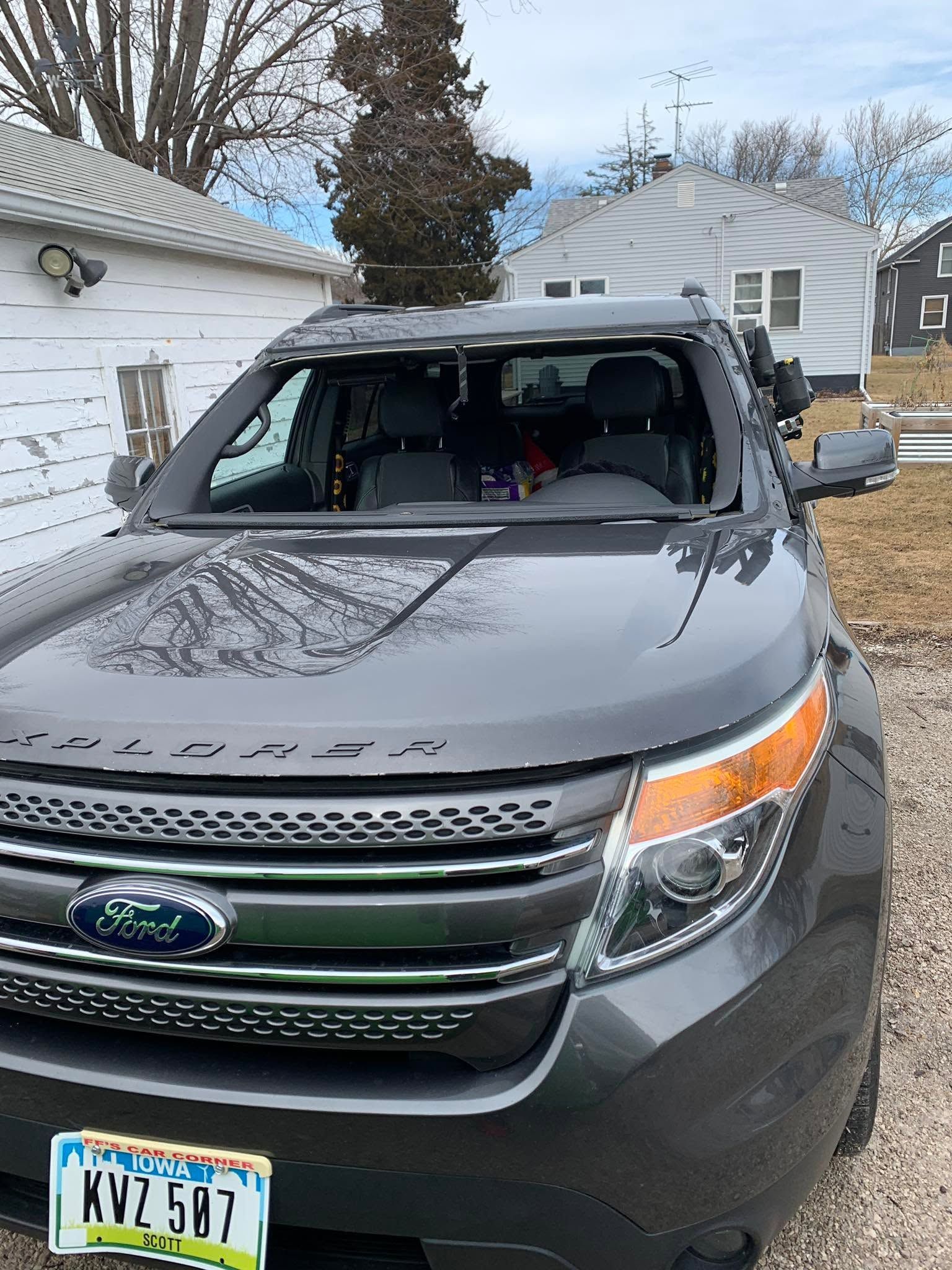 Gray Ford SUV with shattered windshield parked outside a white house on a snowy day