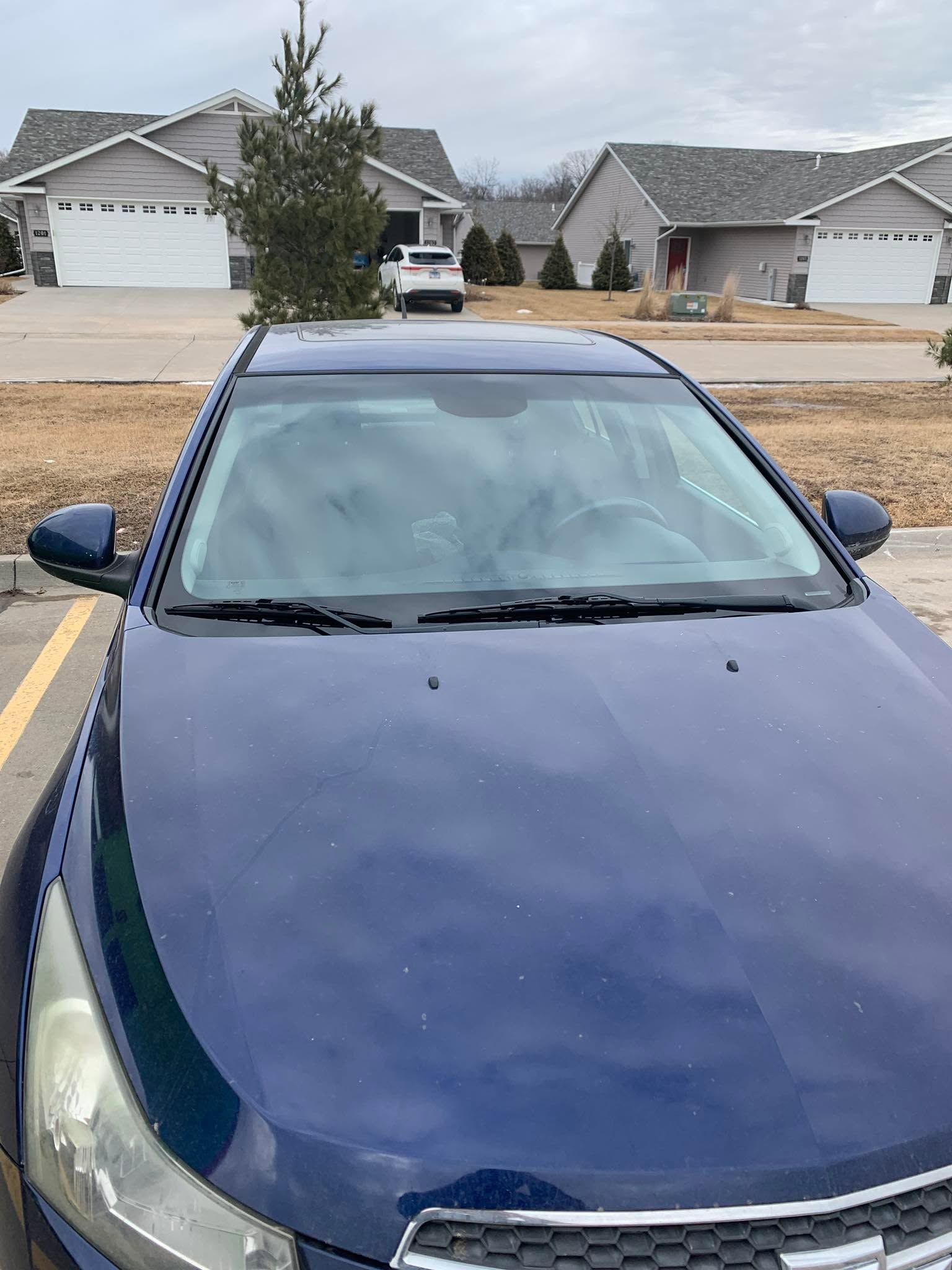 Blue car parked in a suburban driveway with houses in the background