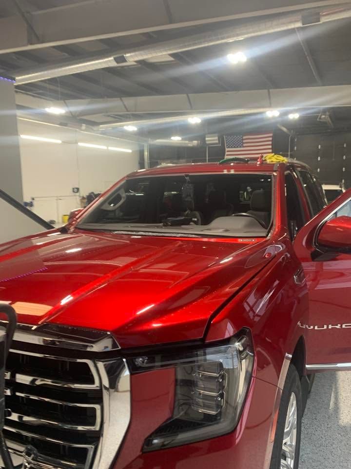 Red pickup truck indoors with chrome grille and headlights, viewed from the front-left.