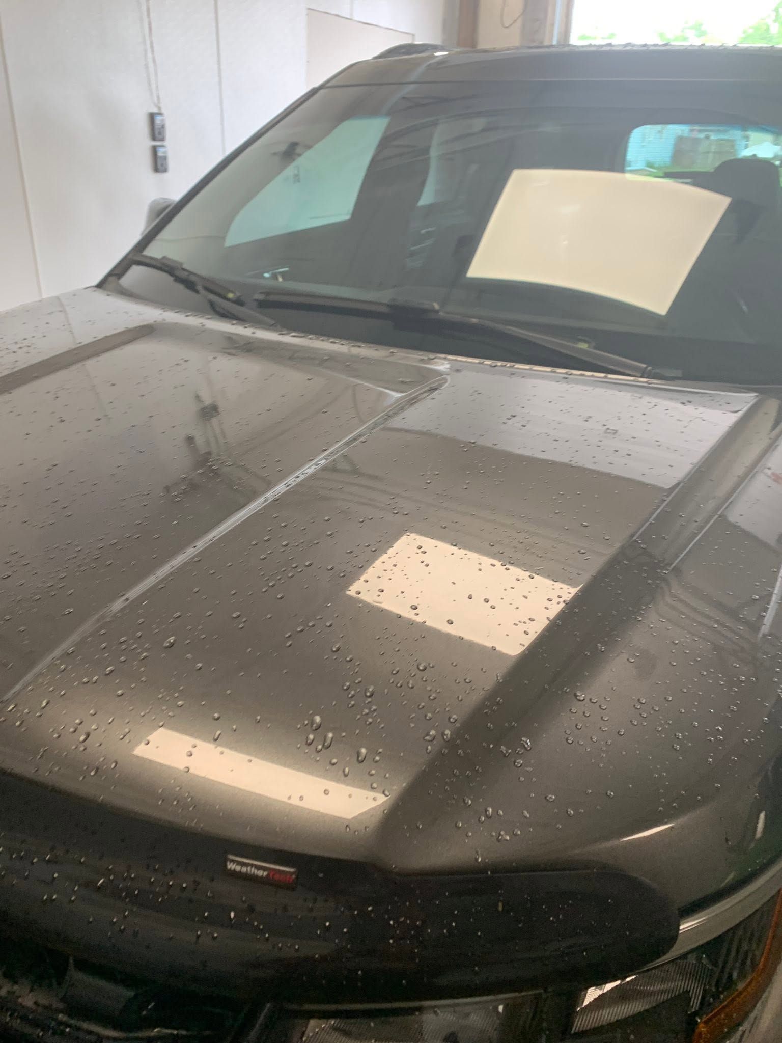Dark gray car parked indoors, wet with raindrops, with a paper note on the windshield.