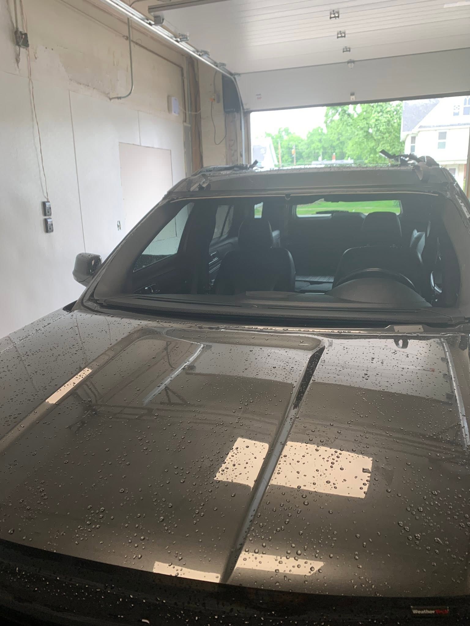 Silver SUV parked in a car wash bay with water droplets on the hood and windshield.