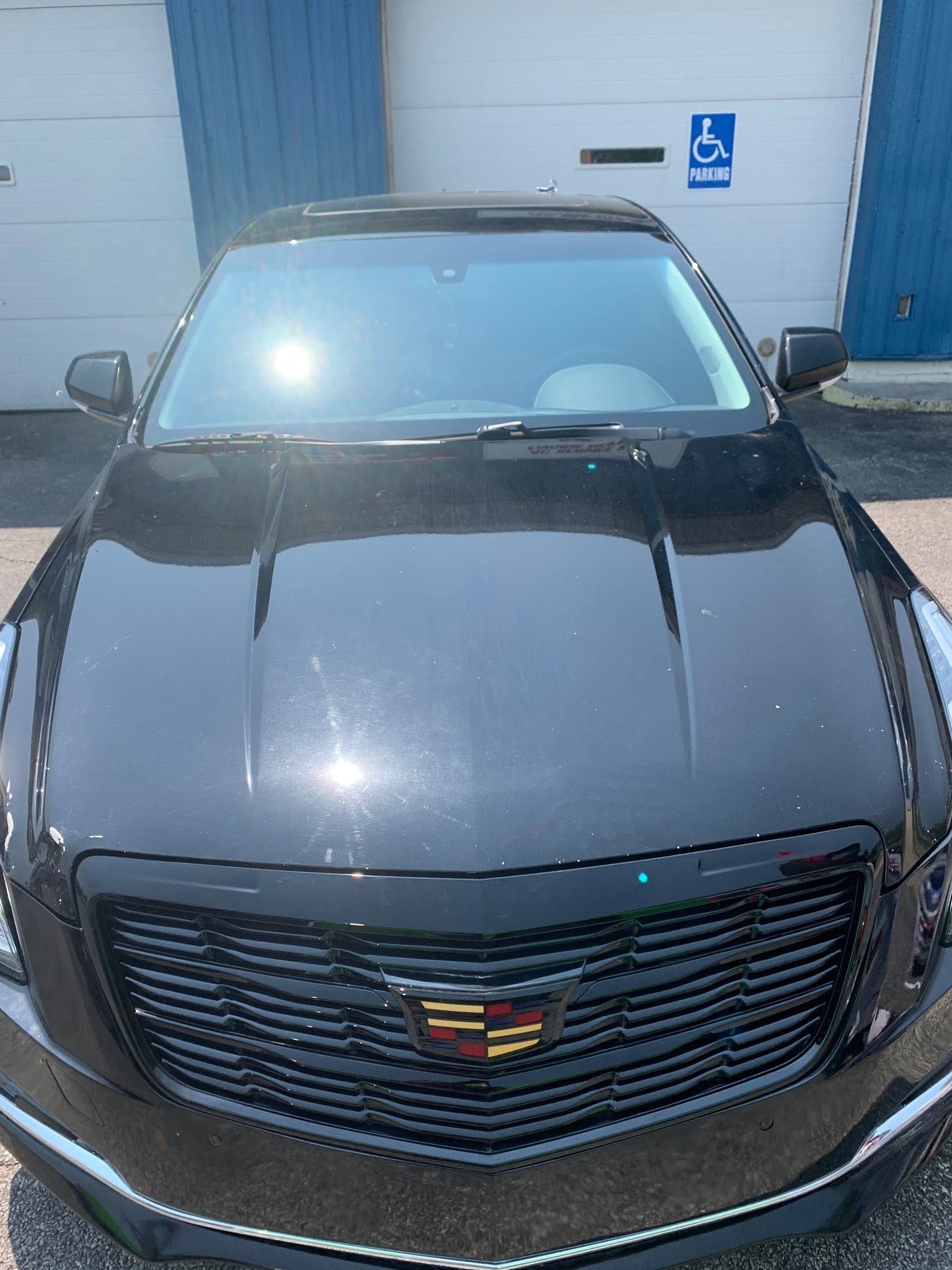 Black Cadillac sedan parked in front of a garage door, viewed from the front.