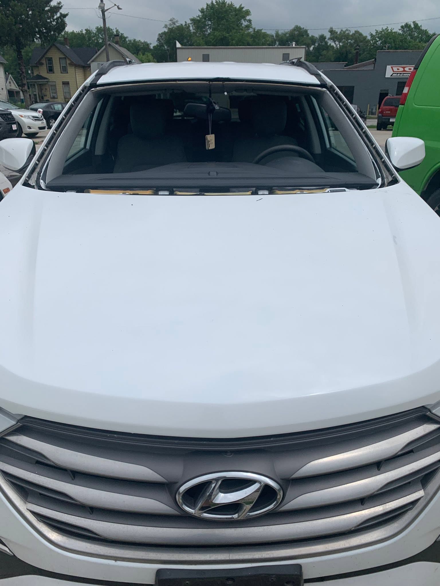 Front view of a white Hyundai SUV parked outdoors with a cracked windshield under cloudy skies