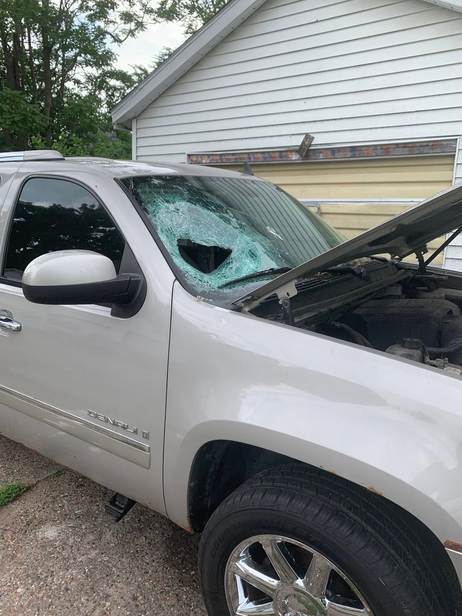 White SUV with shattered windshield and open hood parked beside a house