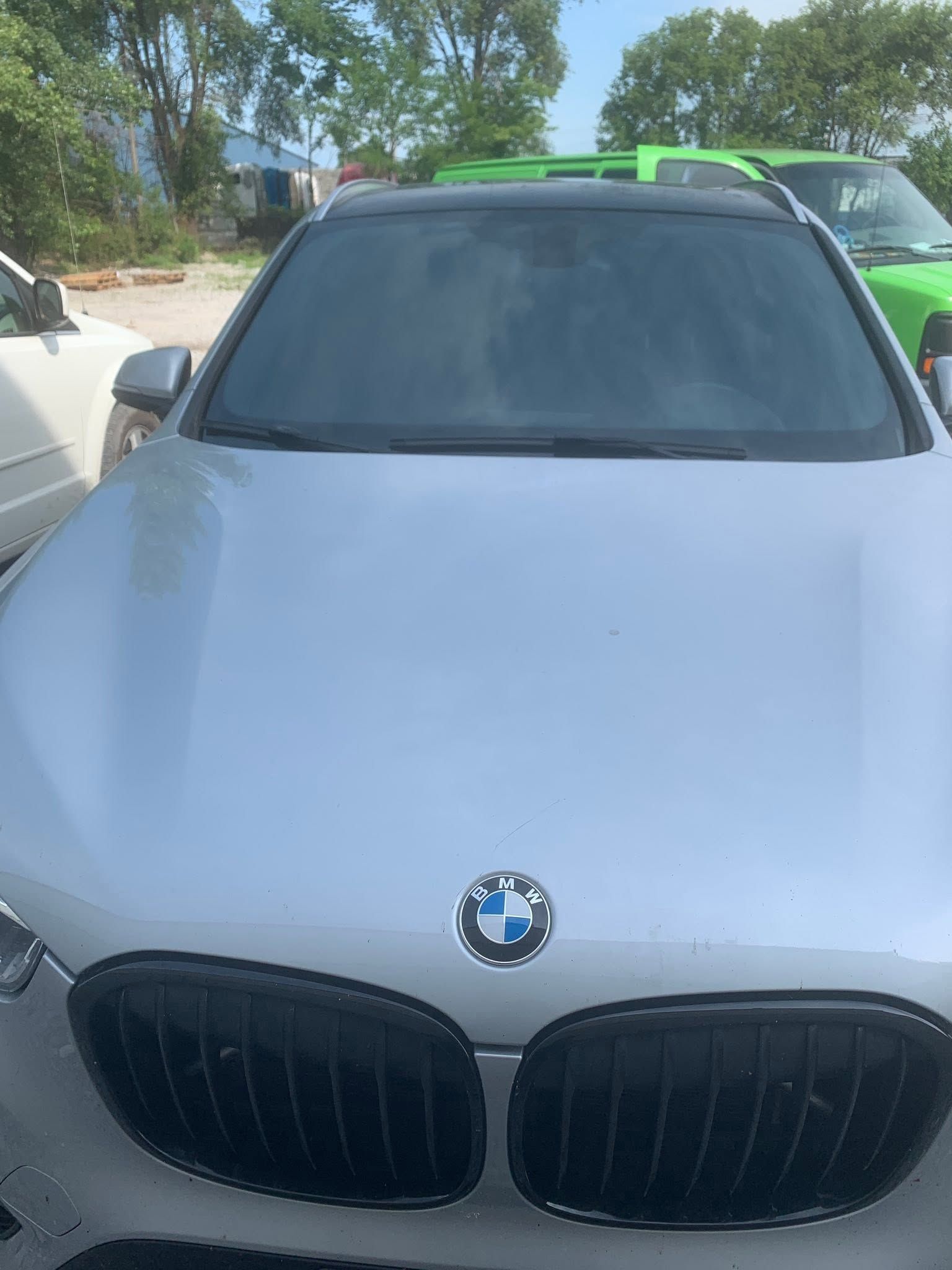 Front view of a silver BMW SUV parked outdoors, with tinted windshield and green roof rails.
