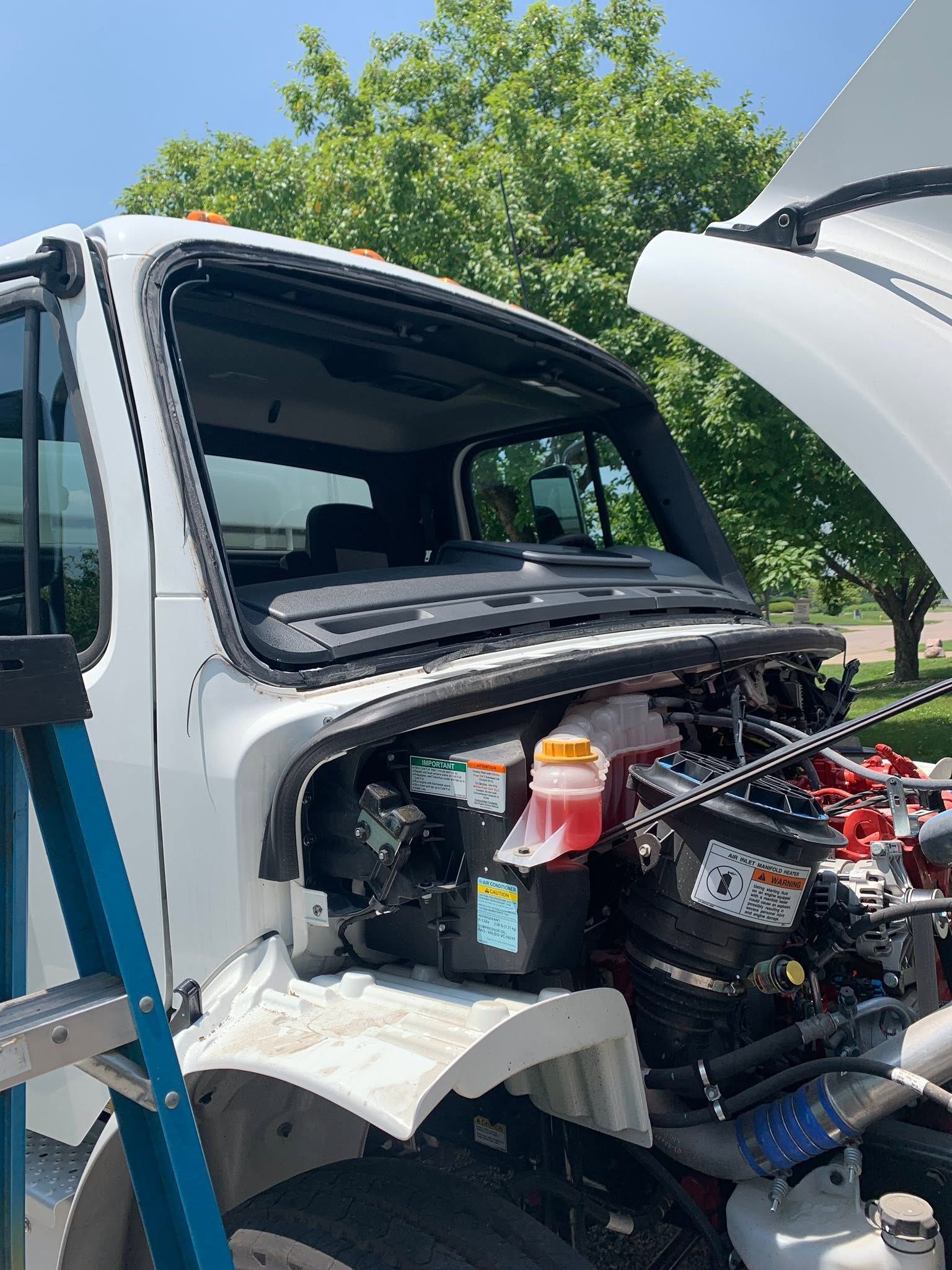 White truck cab with hood open, exposing engine parts on a blue sky day.