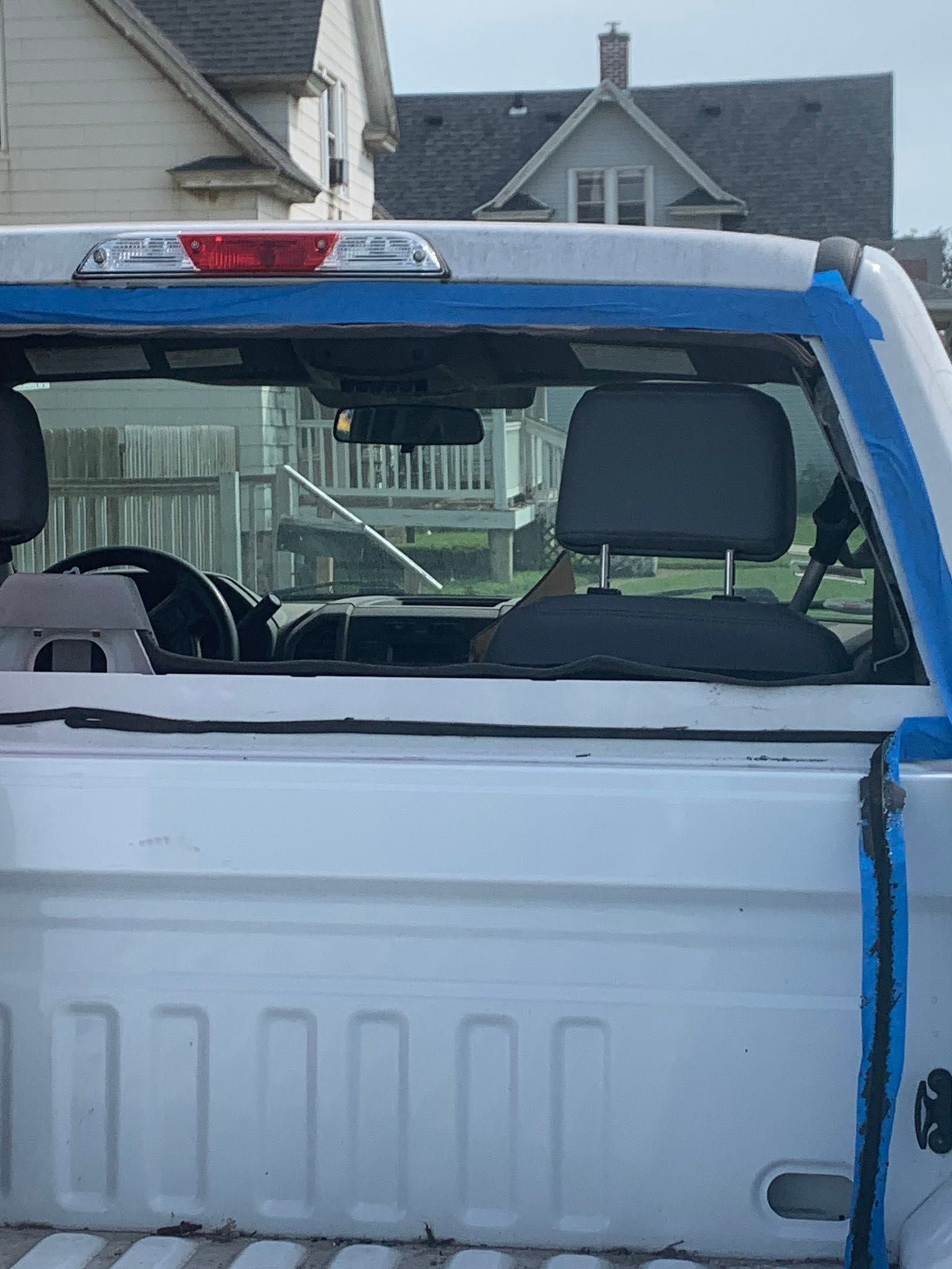 White pickup truck with a blue strap across the tailgate, viewed from the rear in a driveway.