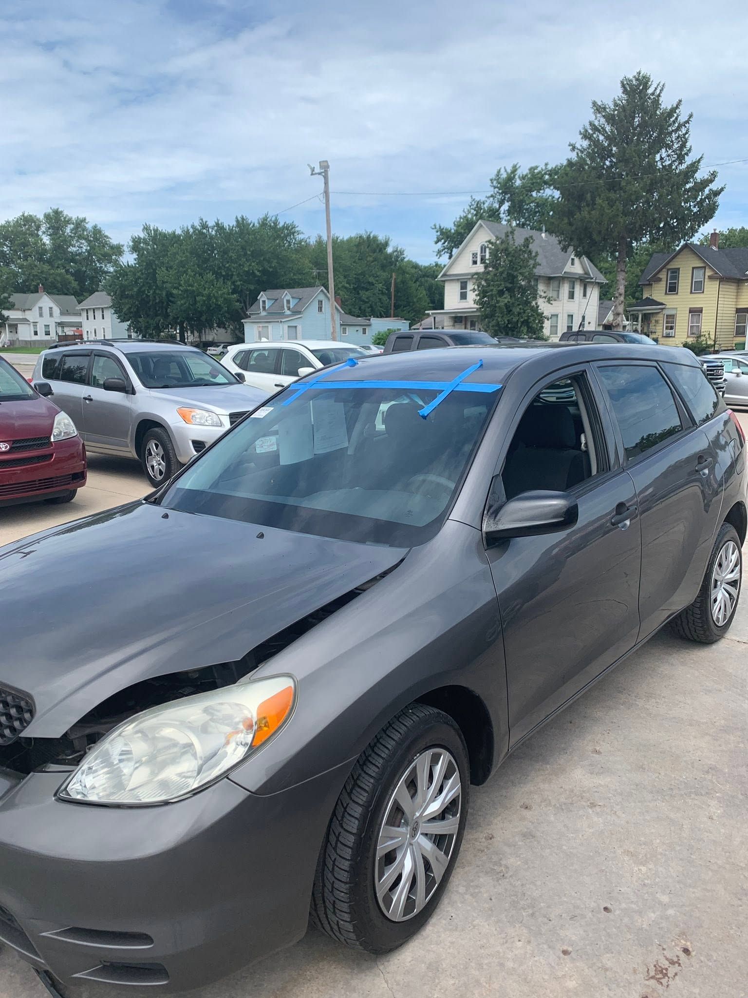 Dark gray sedan parked in a lot, with blue painter’s tape on the windshield and roof