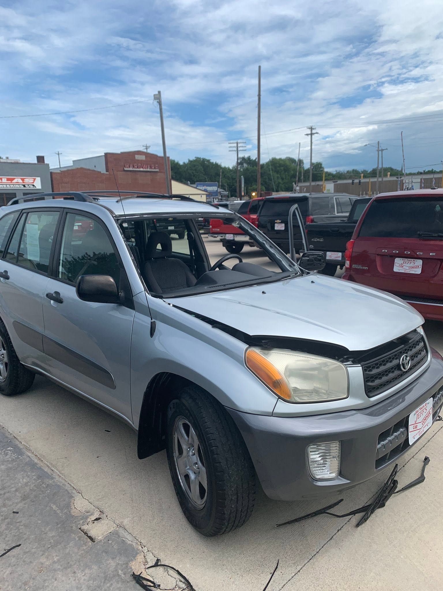 Silver SUV with shattered windshield parked in a lot, with other vehicles and cloudy sky behind it