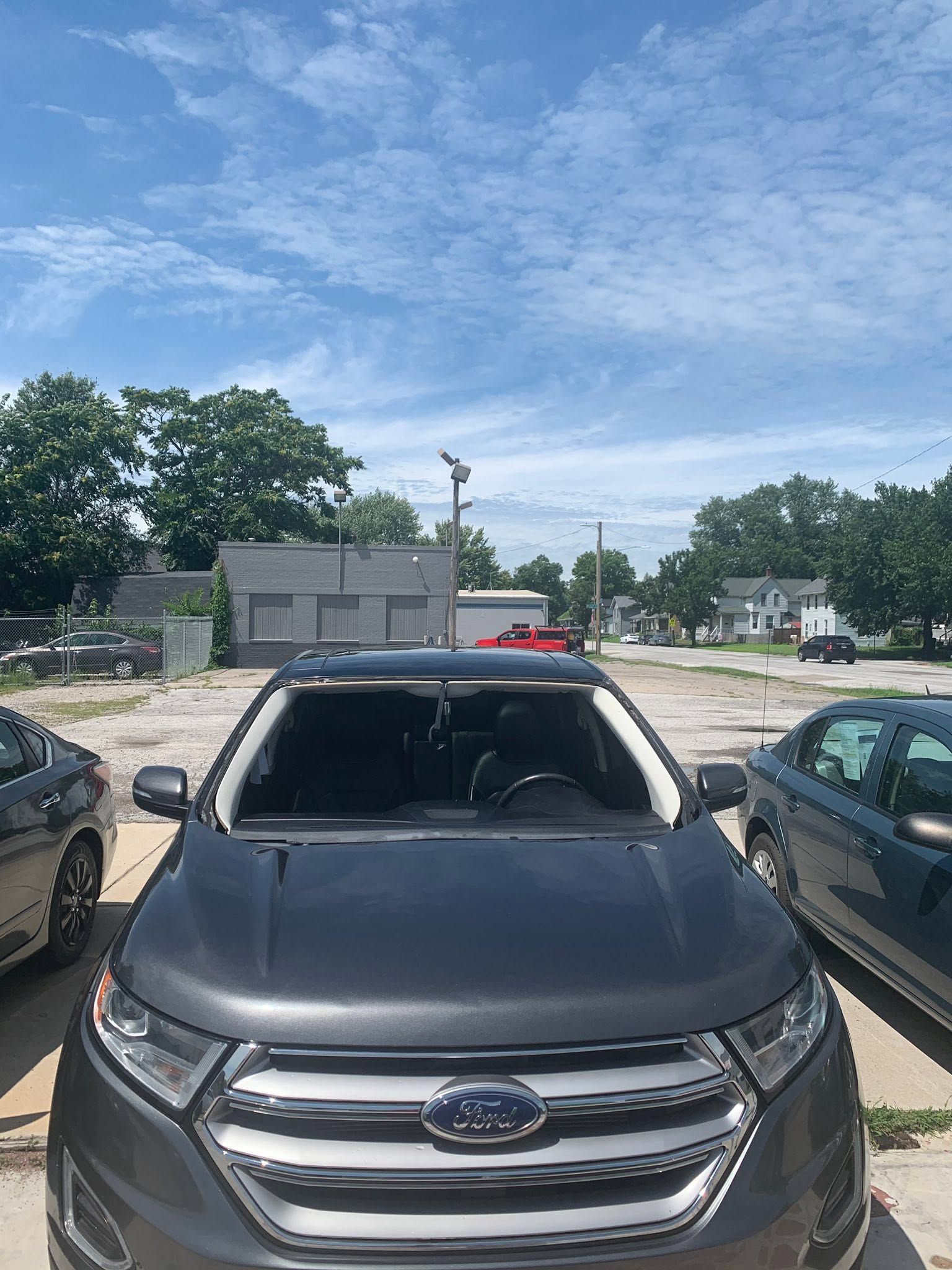 Front view of a black Subaru parked between two cars on a sunny dirt lot.
