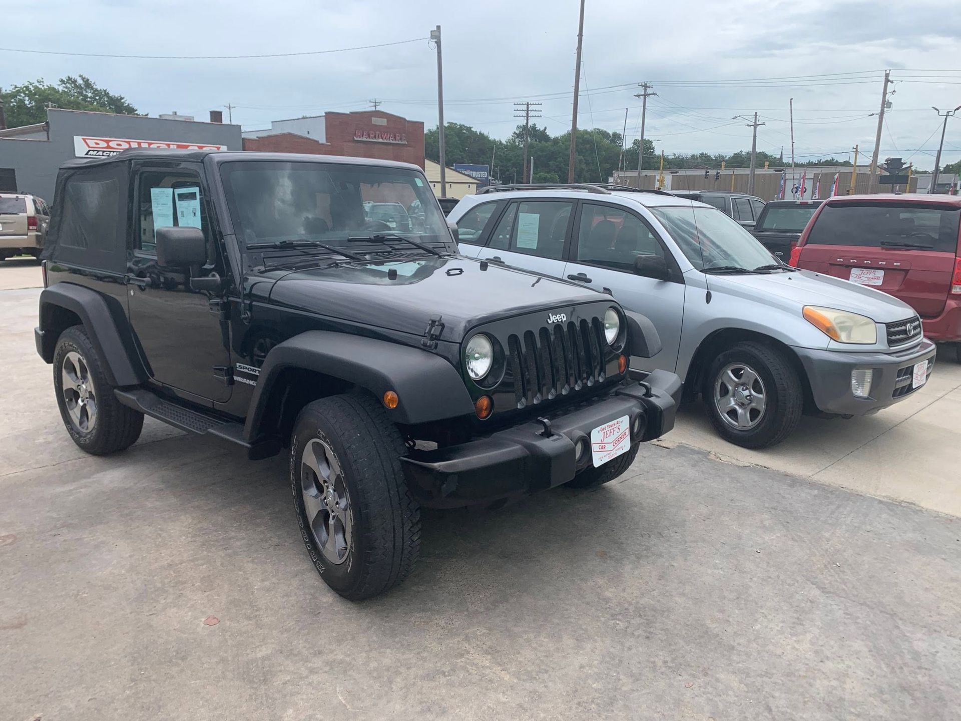 Black Jeep Wrangler parked beside a silver SUV in a lot on an overcast day