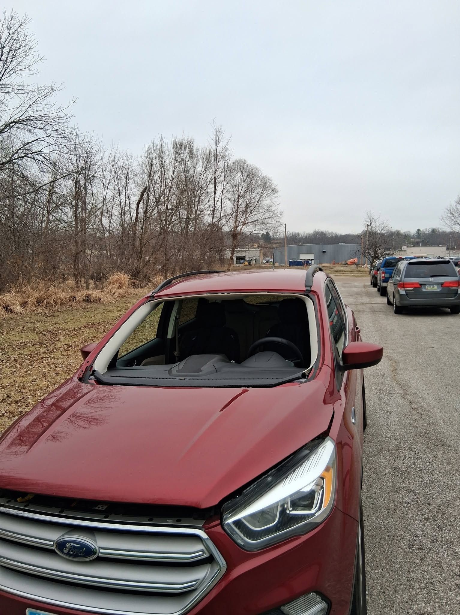 Red SUV with a shattered windshield on the roadside, with several vehicles queued behind it.