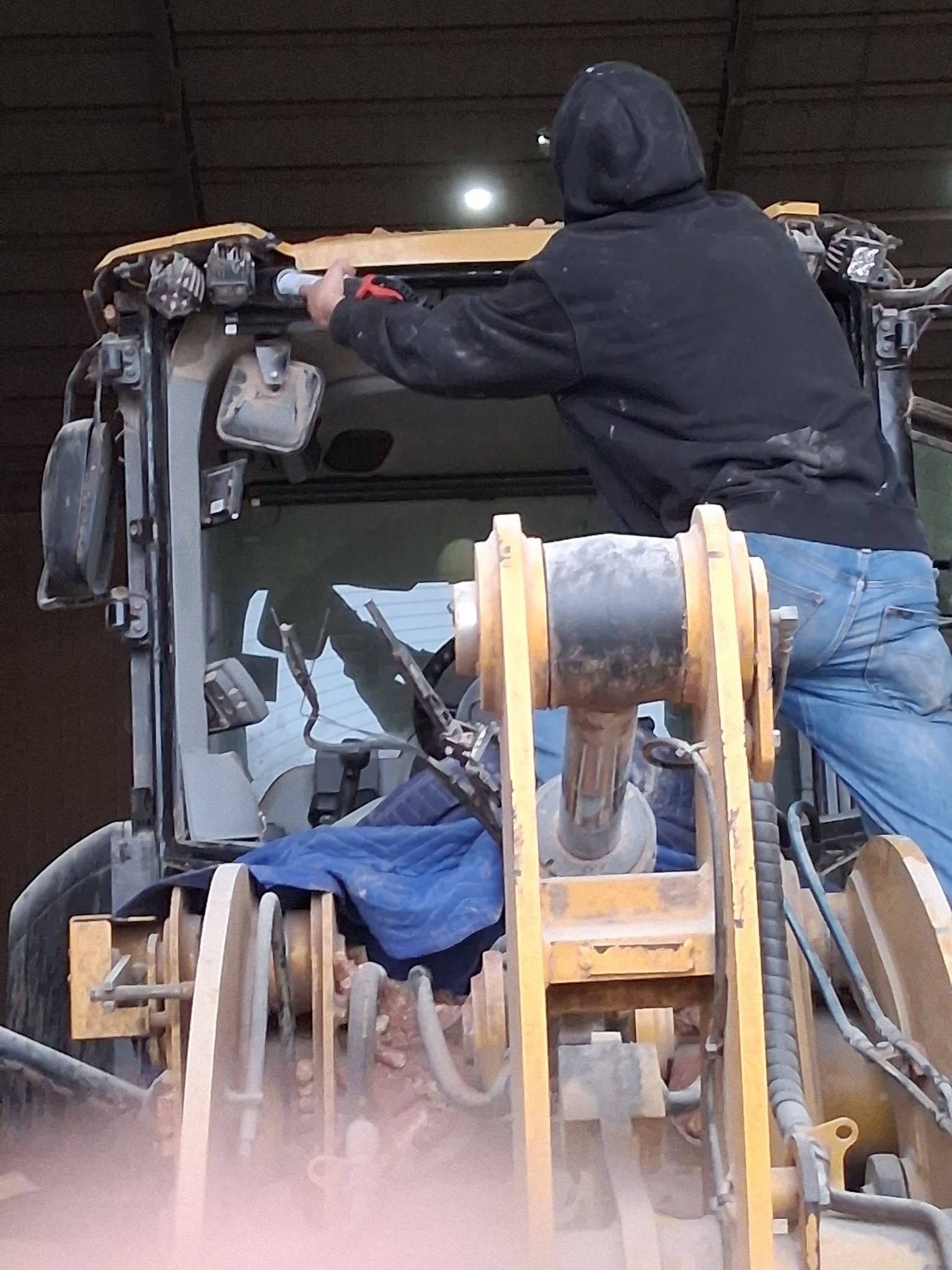 Person in a black hoodie and jeans operating heavy machinery at night, viewed from behind.
