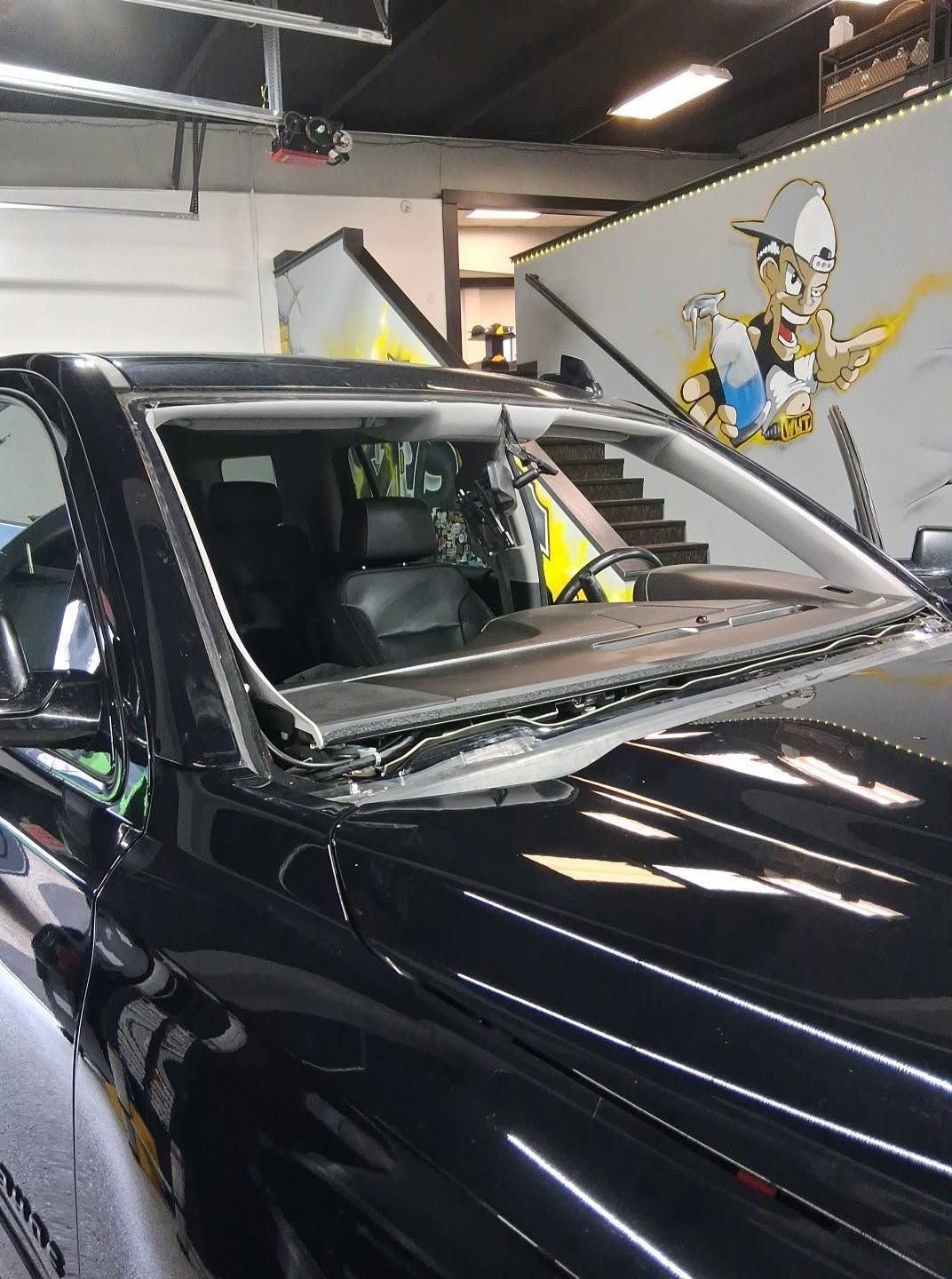 Black car parked in a garage with a Tom and Jerry mural on the wall.