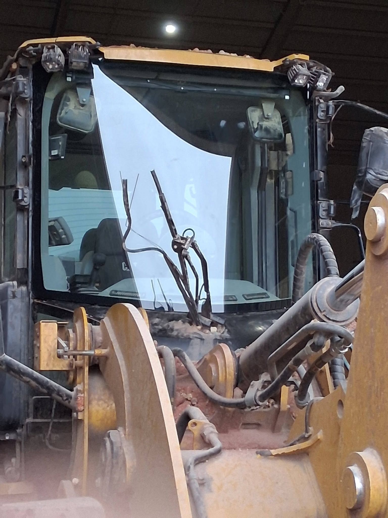 Front view of a yellow construction excavator with a cracked windshield inside a dim garage.