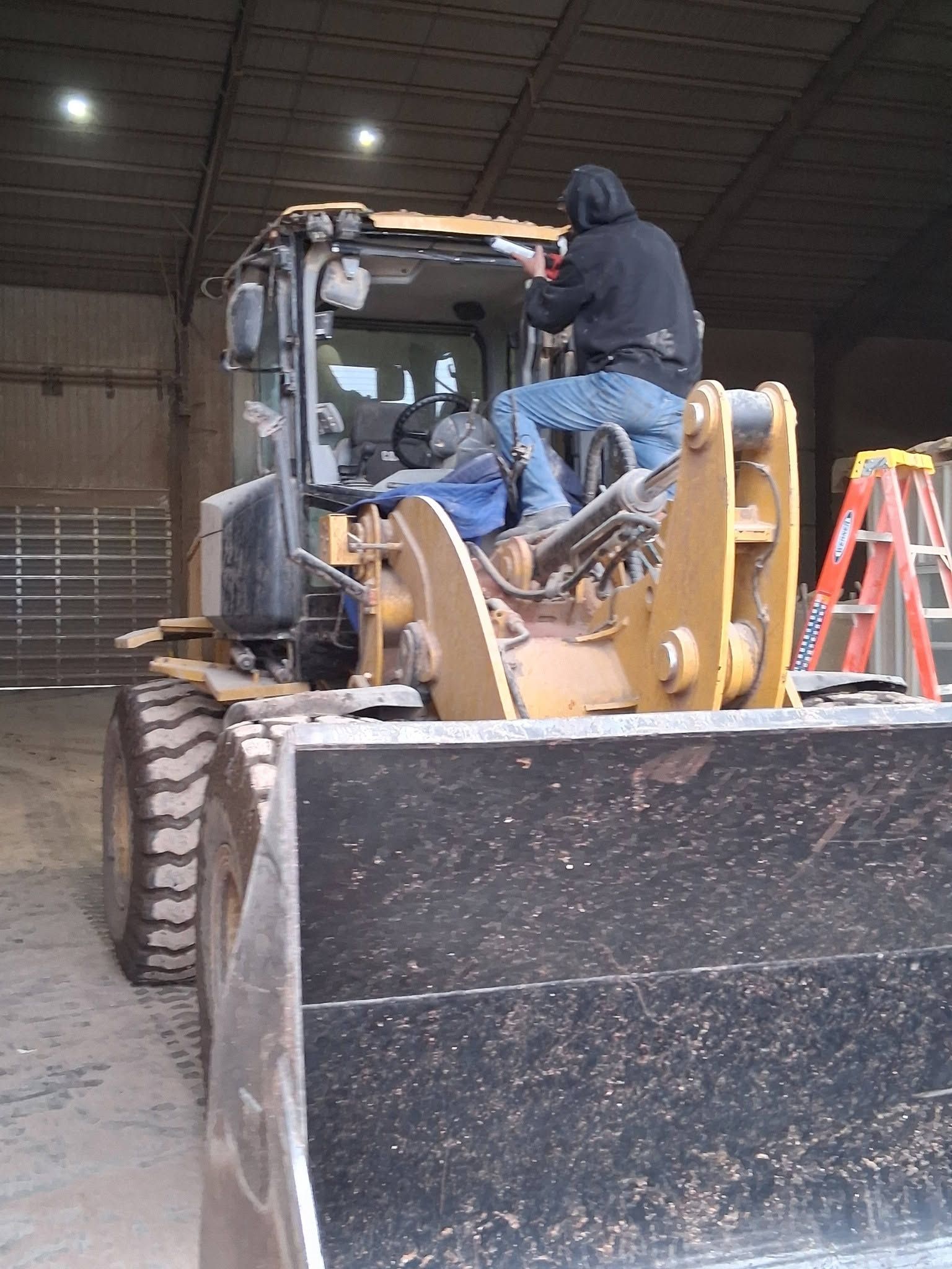 Person operating a yellow bulldozer inside a warehouse, with a large black blade in front