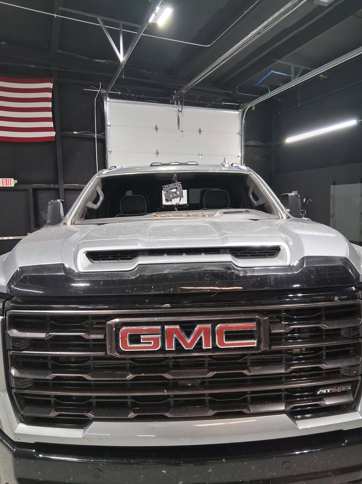 Front view of a silver GMC truck in a garage, with a large red GMC grille badge.